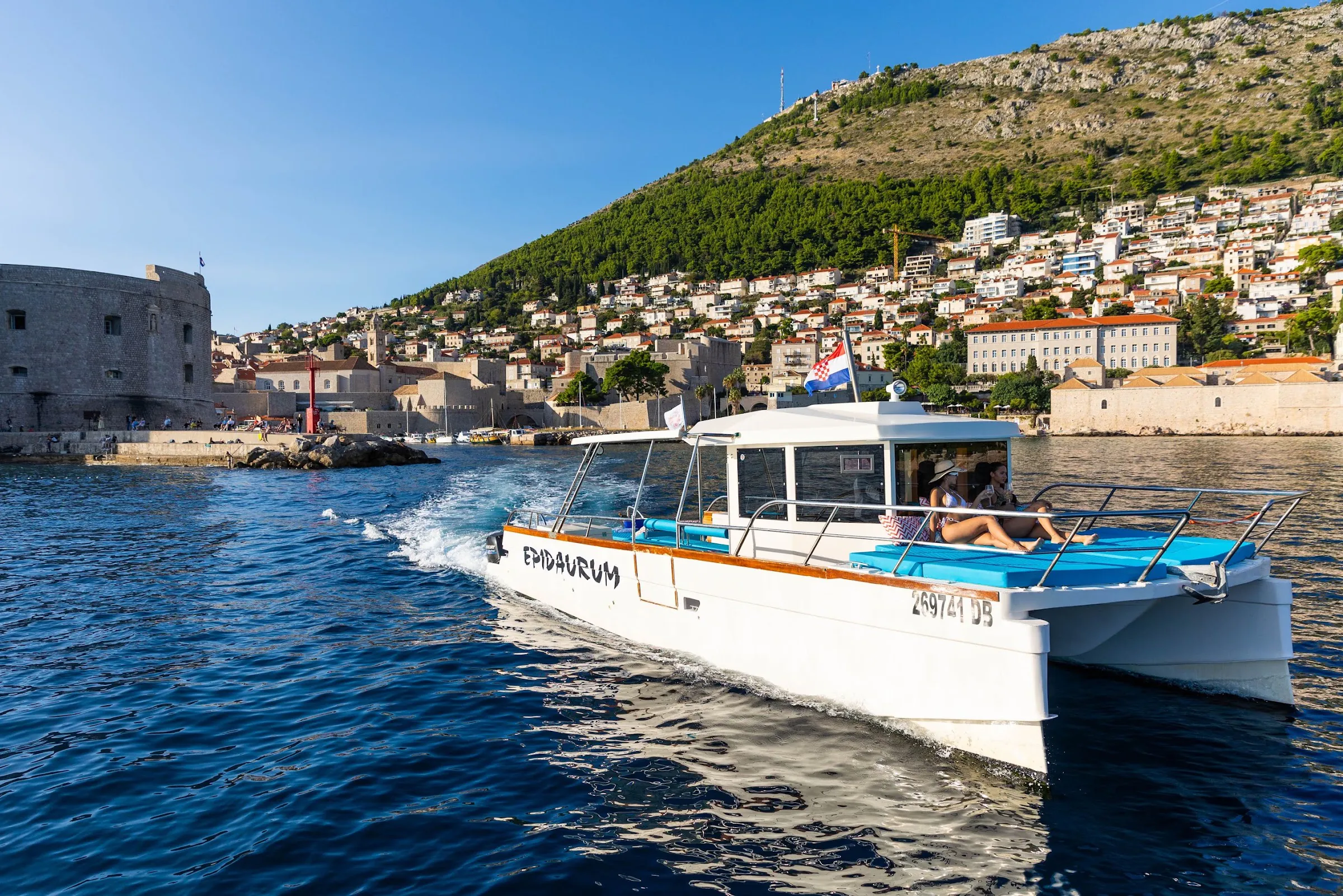 Double-deck catamaran cruising past Dubrovnik Old Town