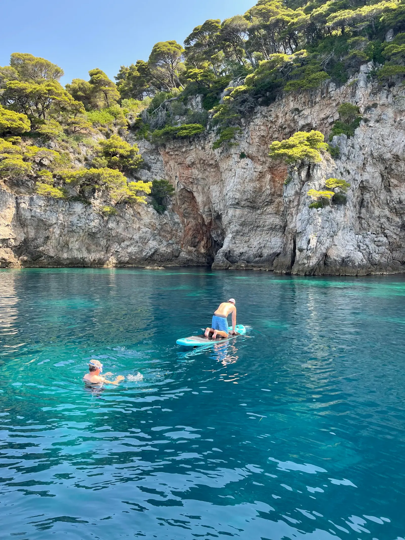 Swimmers and a paddleboard in a turquoise cove under cliffs
