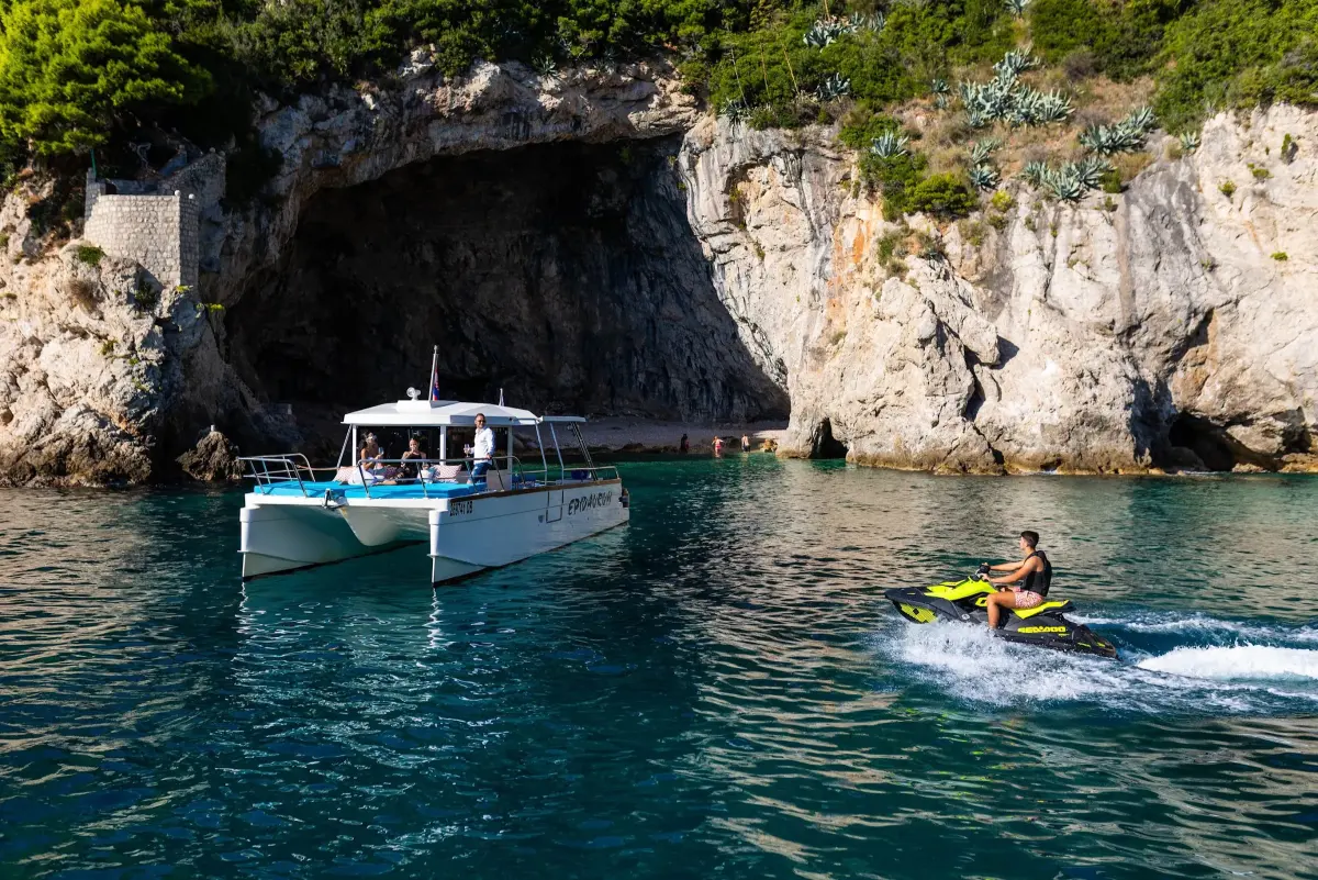 Catamaran and jet ski at the entrance of a sea cave