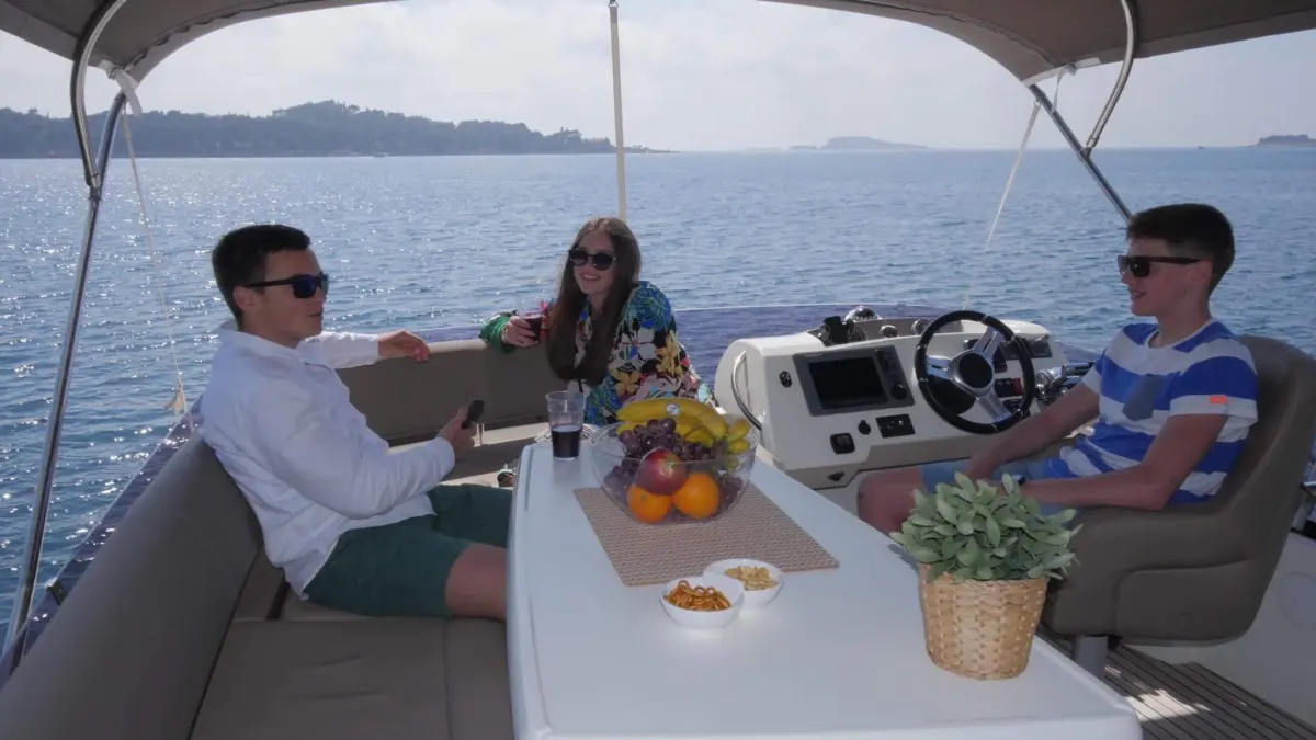 Guests at the table and helm of Amica under the bimini